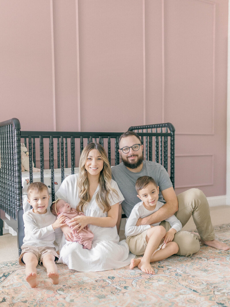 Family sitting in front of crib with newborn baby