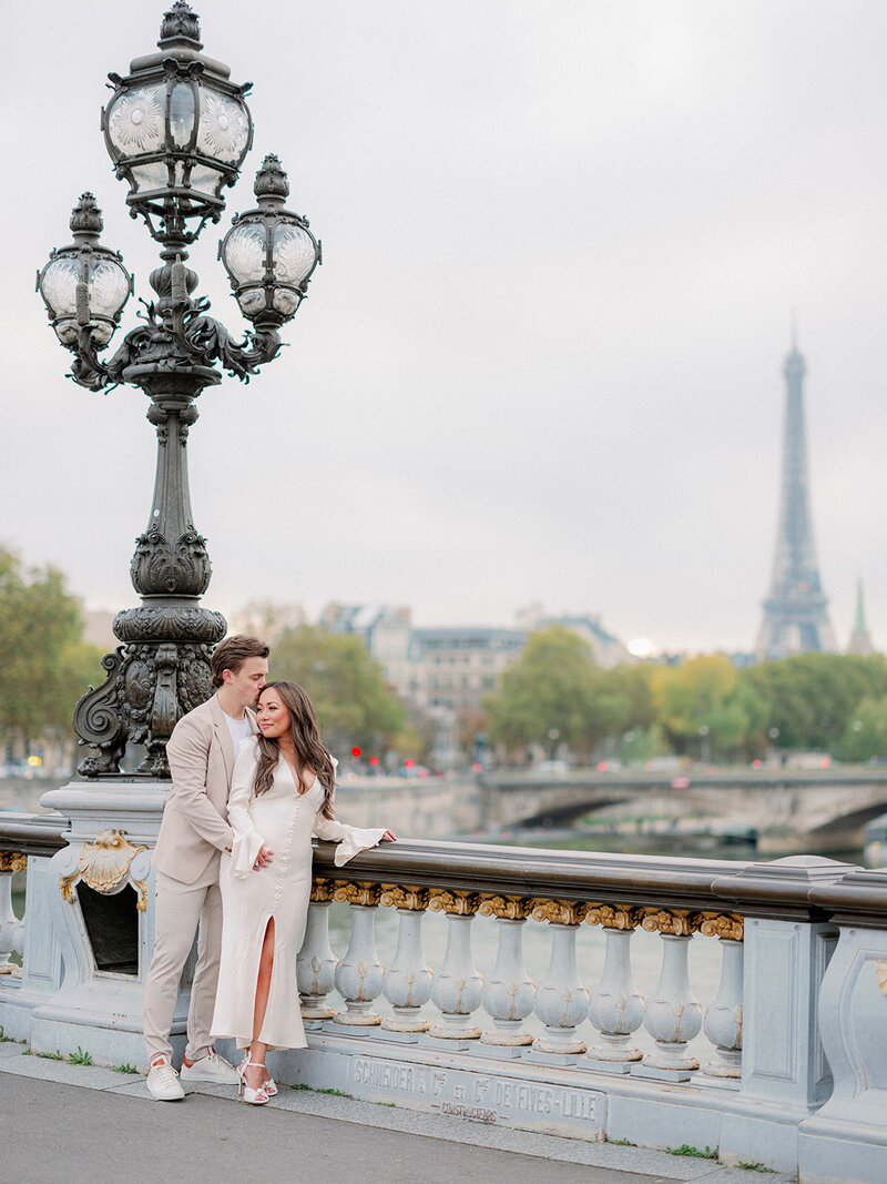 a man and woman on a bridge with the eiffel tower behind them