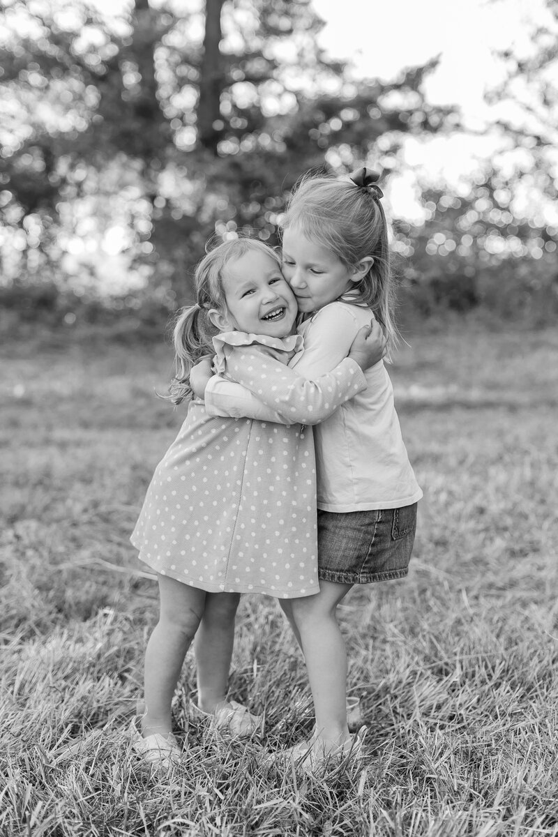 A black and white photo of two sisters hugging outside in the grass by Northern Virginia Family Photographer