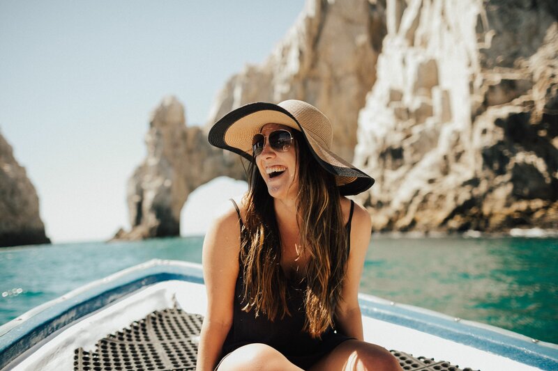 Girl on boat with a large beach hat on and laughing