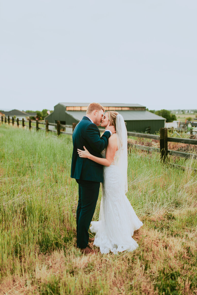 Young married couple kissing on a farm near a fence.