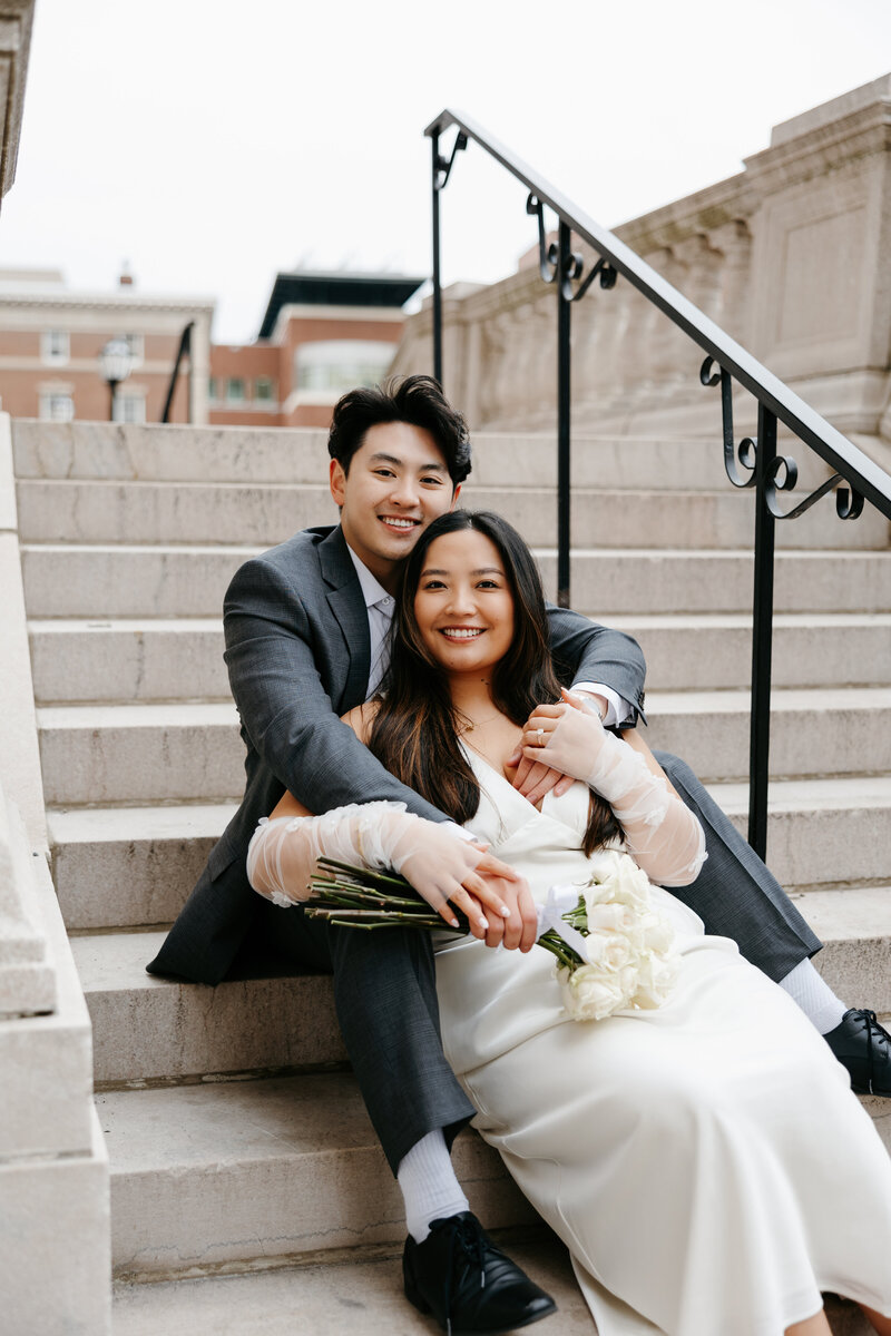 Bride sitting in front of groom outside on a stair case