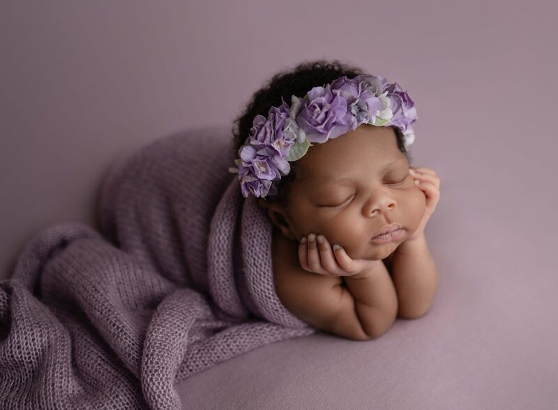 Newborn Baby girls in purple wrap sleeping with hands on chin and purple floral headband. Photographed at Atlanta newborn photo studio.