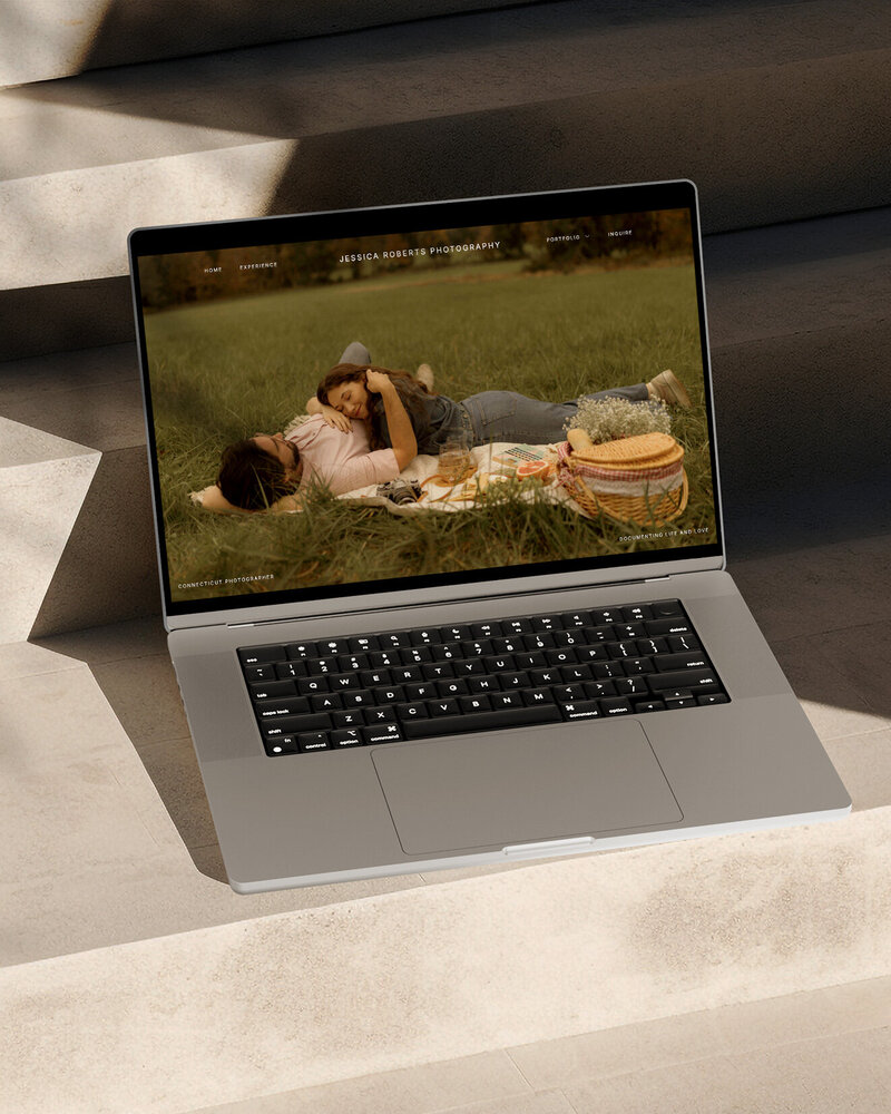 Laptop showing a photography website and two people having a picnic