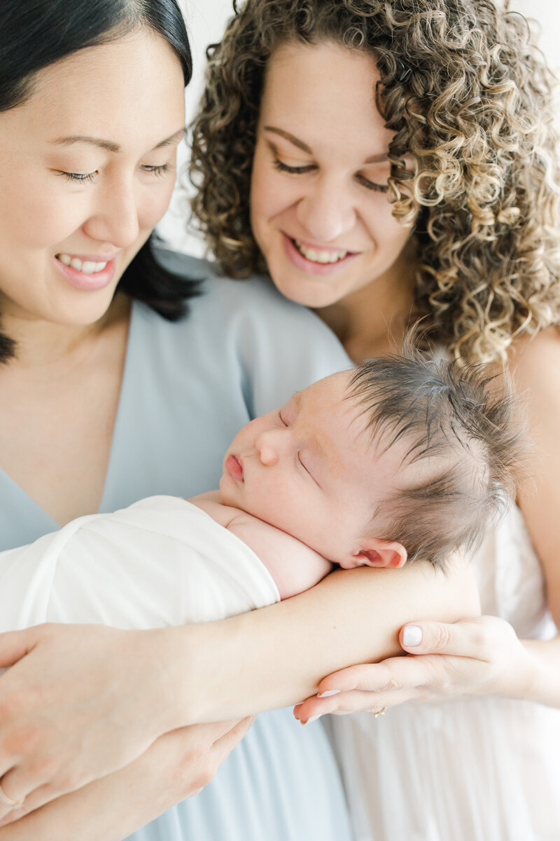 2 mothers embrace their newborn baby son during newborn photography session