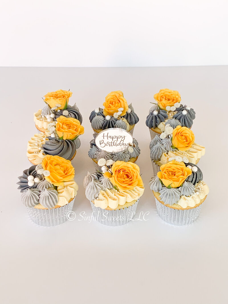 Yellow and grey frosted cupcakes with a happy birthday sign in the center.