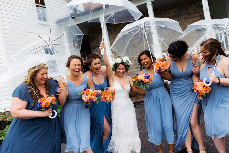 A bride and wedding party laughing under clear umbrellas