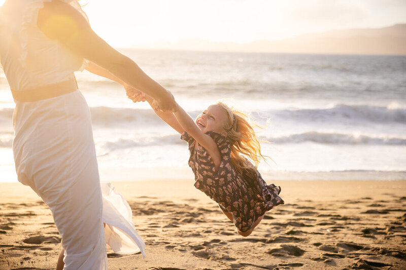 Daughter being twirled around on a San Francisco beach during golden hour. 