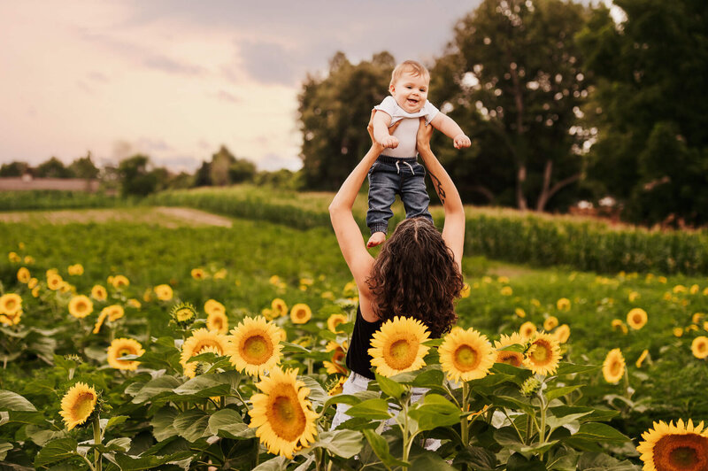Mom and her son being held in the air having fun in the Sunflower fields near Toronto at The Apple Orchard.