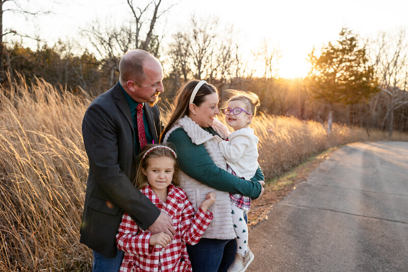 Family session taken in December of a family of four standing in a road at sunset. 