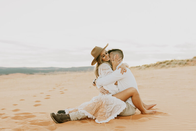 couple sitting and hugging in sand dunes in southern utah for their elopement, photo by photographer kaitlyn neeley