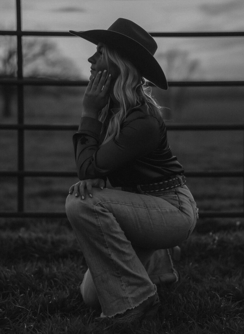 Black and white side portrait photo of a girl in western attire, kneeling down.