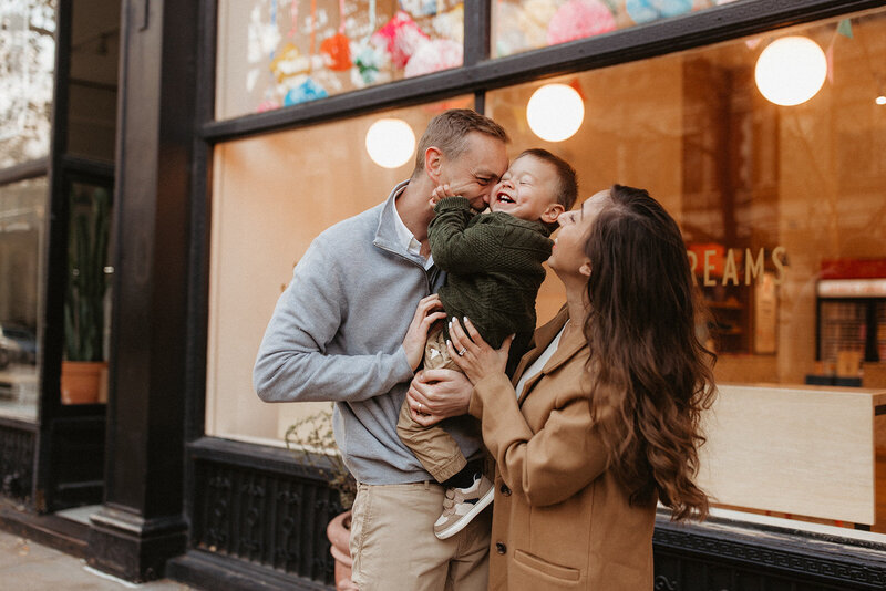 Brunette mom and blonde dad tickling their son in front. of ice cream shop