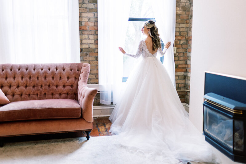 Bride in a white wedding gown gazing out the window at Aster Café in Minneapolis, captured by Minnesota wedding photographer Toly Dzyuba.