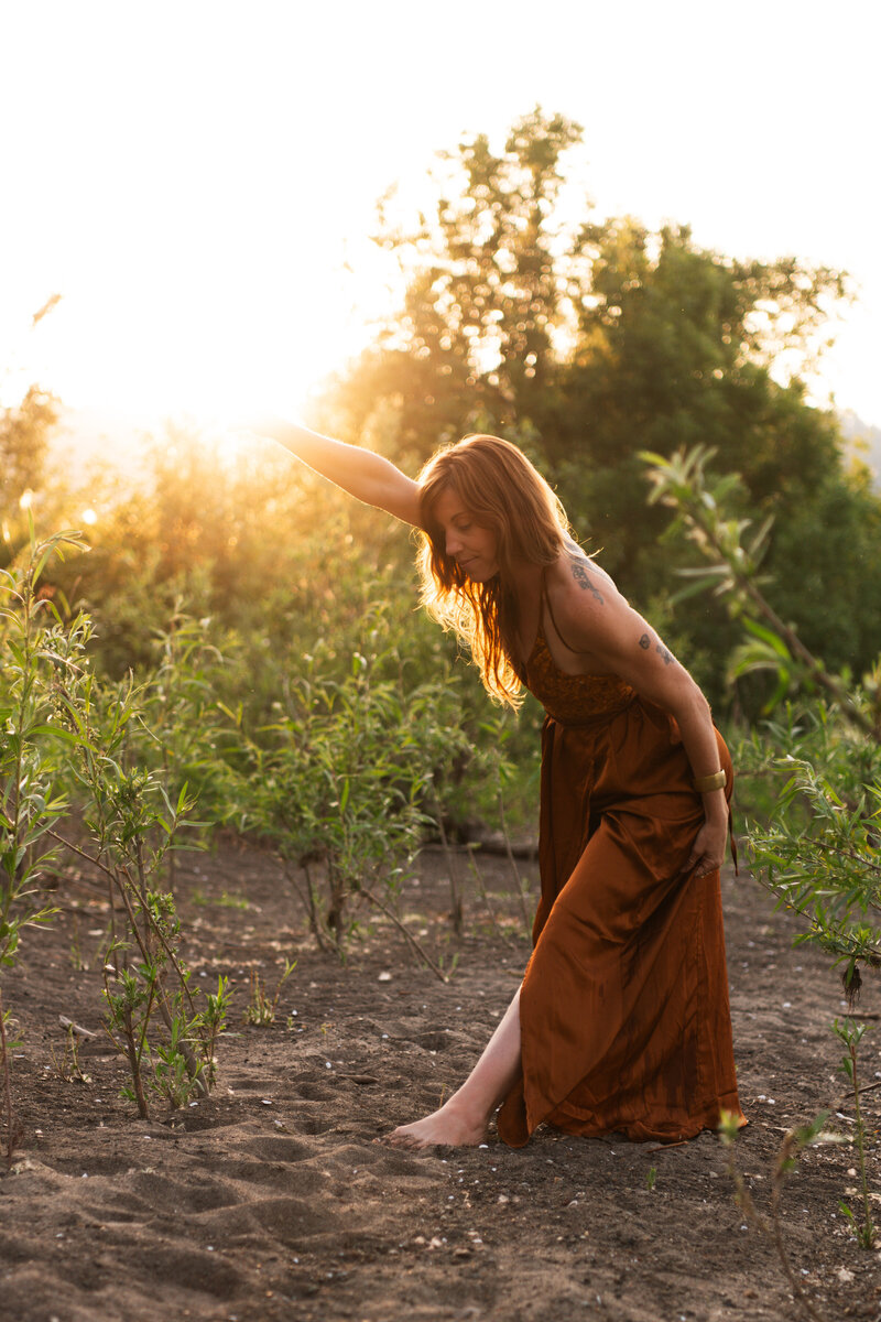mentor, healer, guide with arms out wide in a green field with a sunburst behind her
