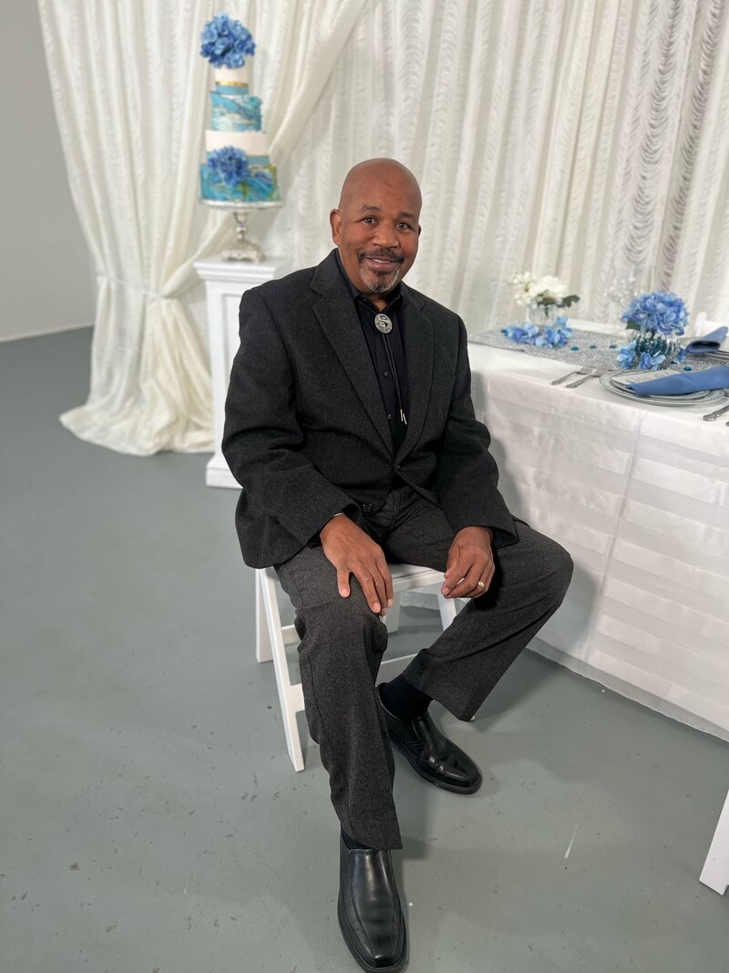 Wedding planner in black suit sitting in front of blue decorations