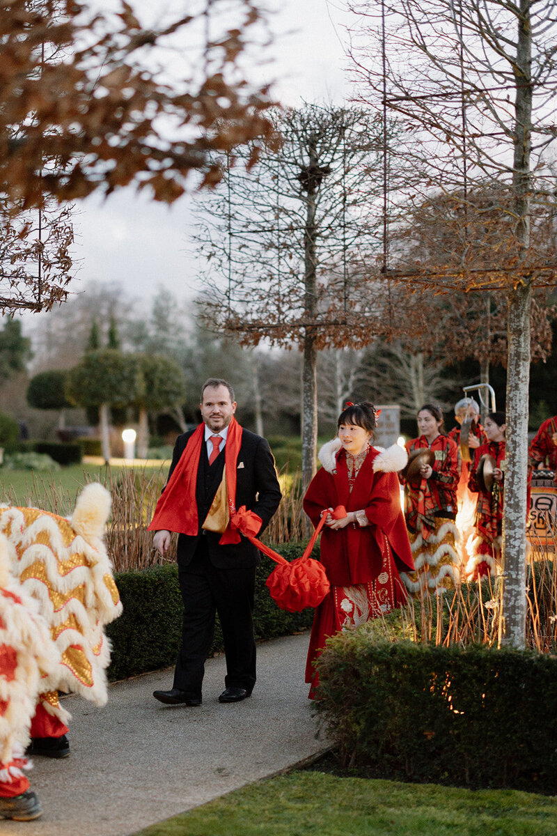 Chinese bride and French groom walking in front of dragon dancers at their fusion wedding at Monkey Island in the UK.