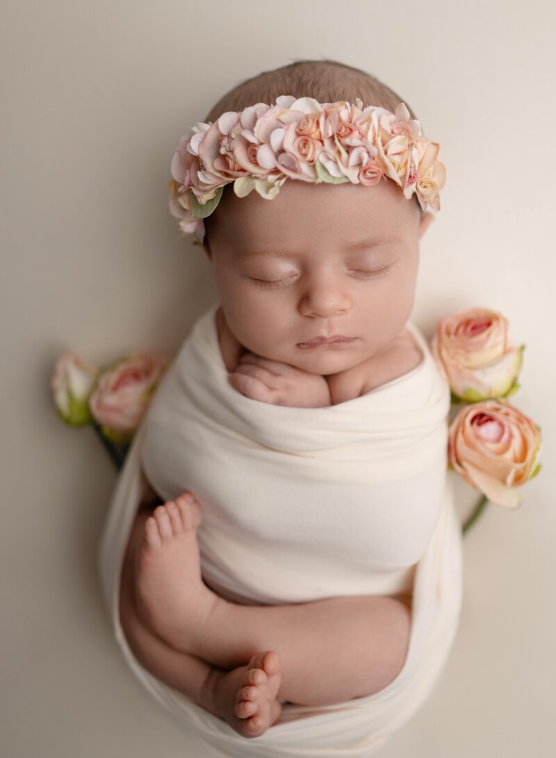 Baby girl swaddled in cream wrap, sleeping, with roses by her side. Photo was taken by Jenni Nikki at her Woodstock studio near Atlanta GA