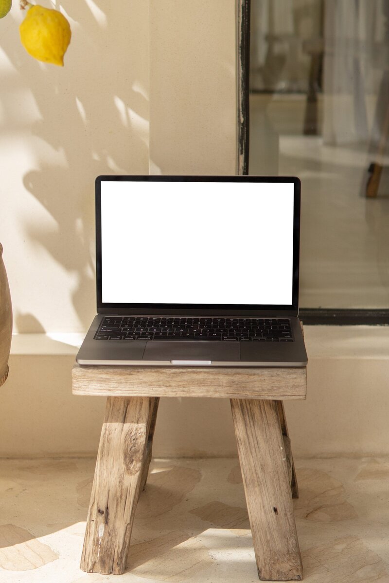 Amare Mockup Shop: MacBook mockup elegantly placed on a wooden chair in a boho-style environment, harmonizing technology with rustic charm.