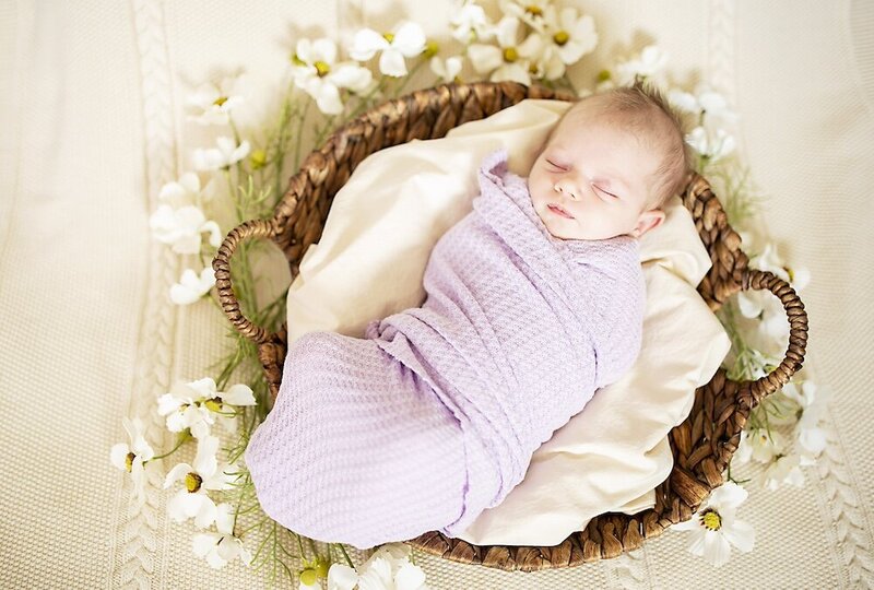 Newborn girl is swaddled in lavender blanket lying in a basket near Fort Rucker