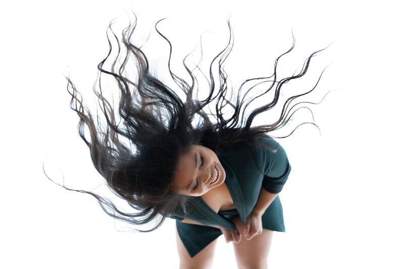 A dynamic boudoir photograph of a woman flipping her hair, wearing a chic green outfit, captured with a sense of movement against a clean white backdrop