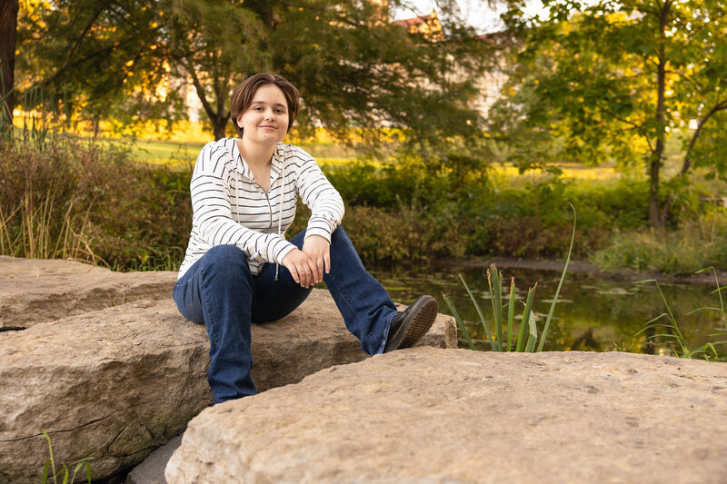 Senior photo session of Amelia sitting on a rock at Potter Lake in Lawrence, KS | Senior Photographer in Lawrence, KS