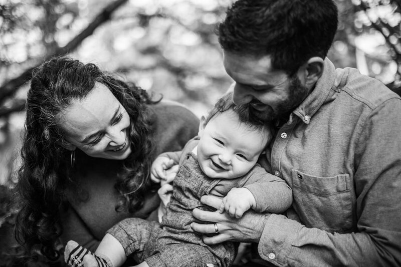 Young boy in parents' lap laughing and parents smiling looking down at him. Image by Alyx Jones Photogrpahy. 