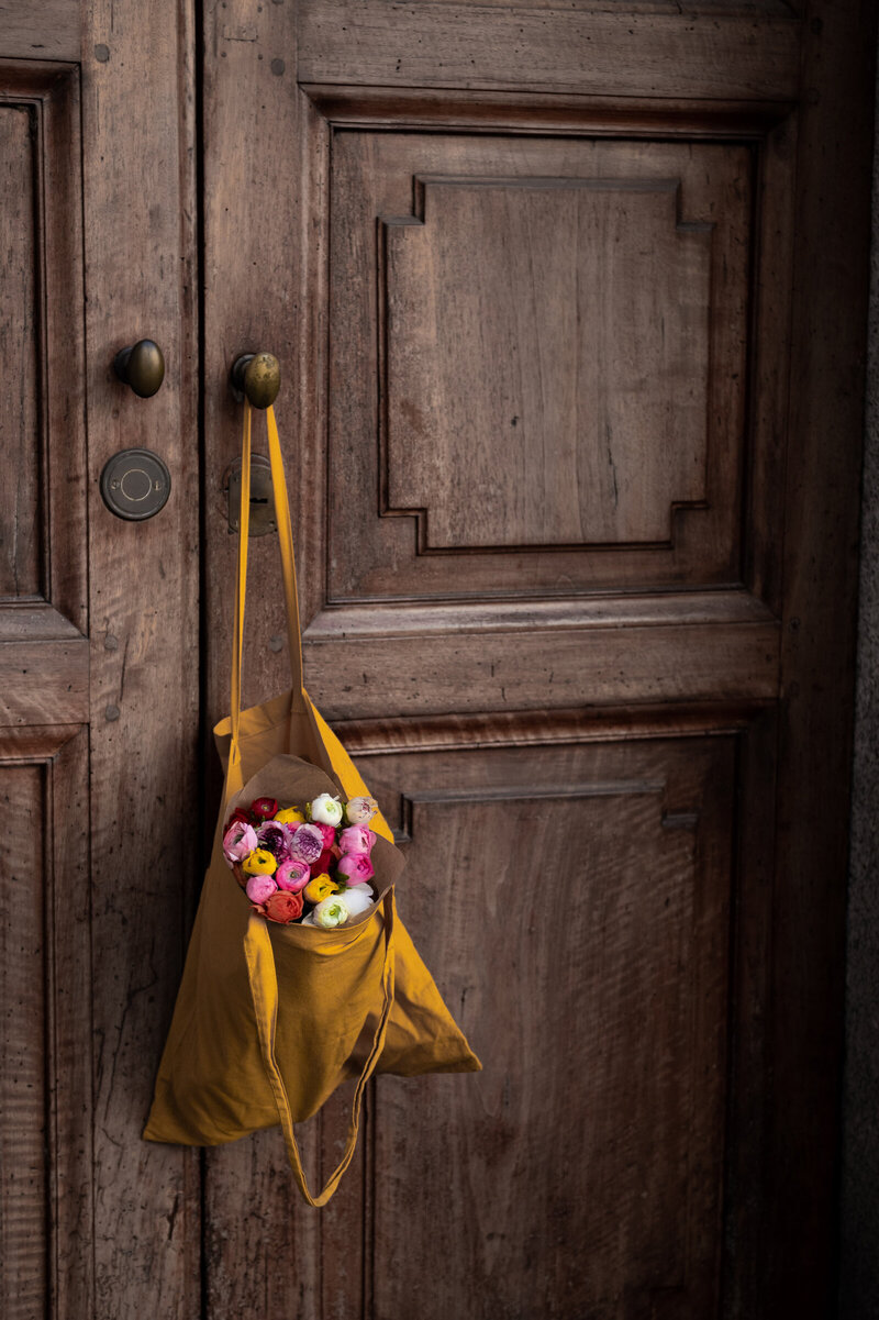 Bright bouquet of flowers in a yellow bag hanging on a wooden door knob