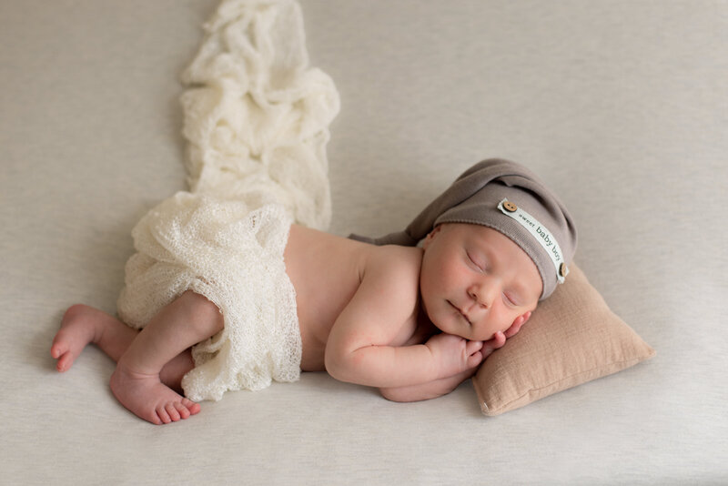 Newborn sleeping on their side with invory mesh wrap and tan slouchy hat that says Sweet Baby Boy