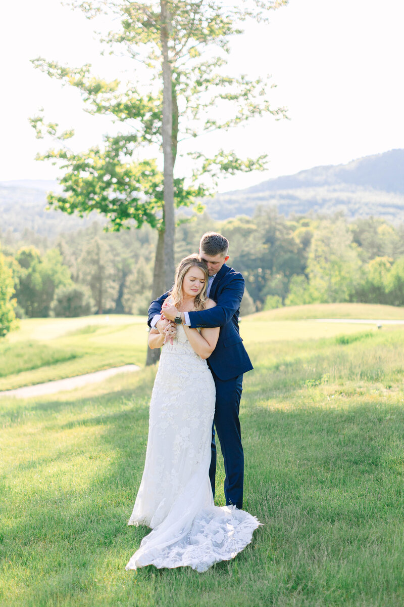 Bright and light wedding photo of a man and woman hugging outside in a suit and wedding dress with trees in the background