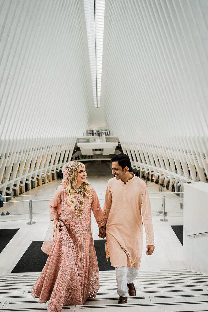 Engagement photo of couple walking and smiling inside the Oculus in New York City – by Alex Kaplan Photography