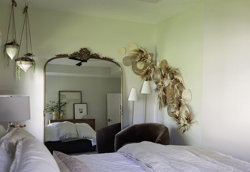 Delicate bedroom with pink blankets, a suede chair and a gold antique mirror.