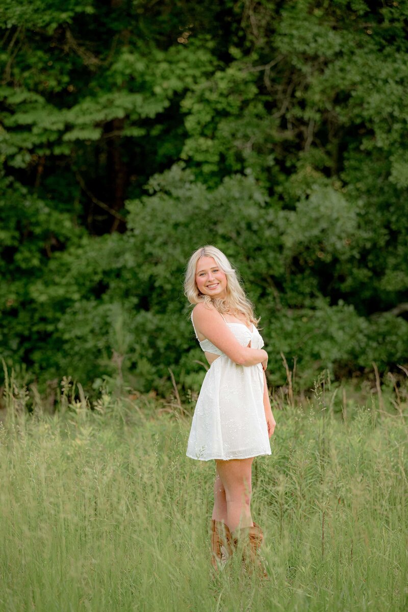 grad from MRHS poses in grassy field wearing a white dress 