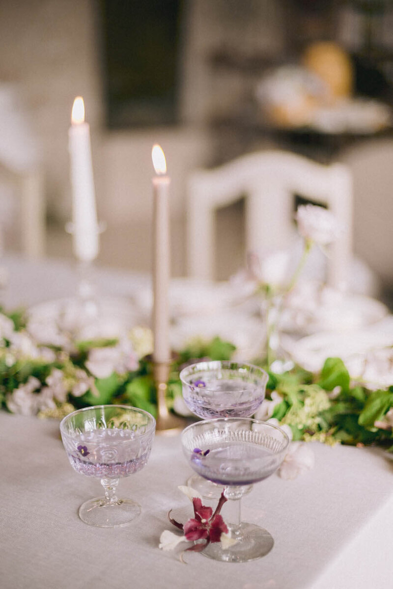 Purple cocktails in glasses on a table with tall candles by San Diego wedding planner Sisti & Co.