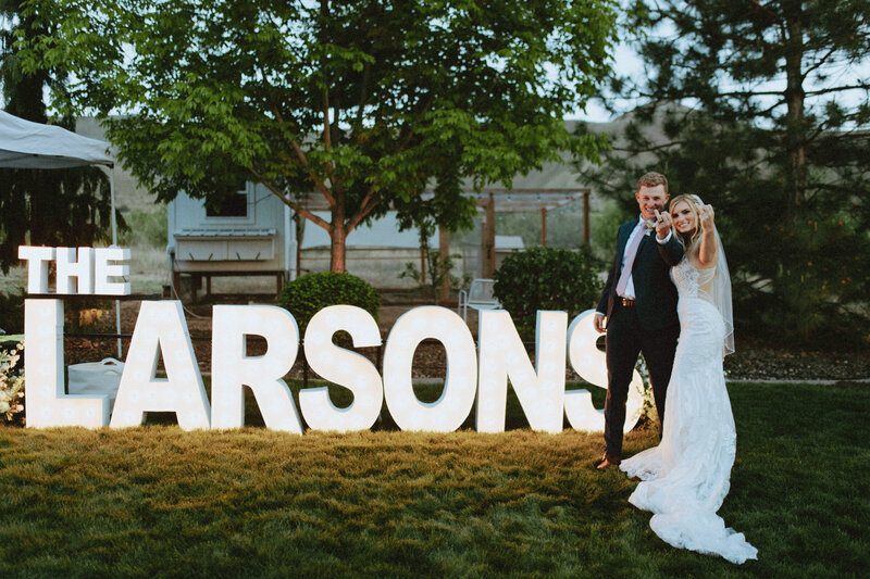 The Larsons stand in front of a large sign that says "The Larsons" holding up their ring fingers like they are flipping off the camera. Classy.