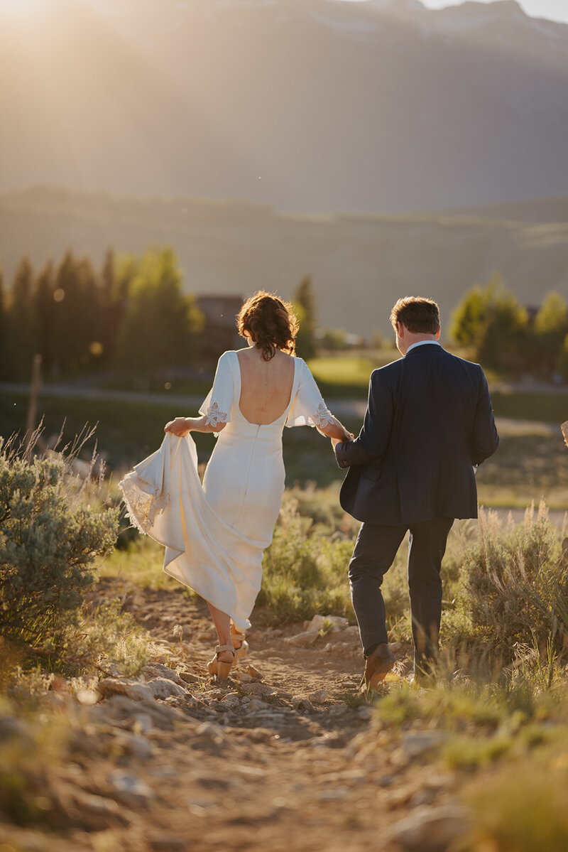 Wyoming wedding Couple walking in field as wedding dress blows in the wind