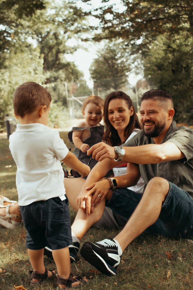 Family of four with two small children sitting and smiling and playing outdoors in a park – representing relationship and parenting support with Freedom Couple Counselling in Melbourne.
