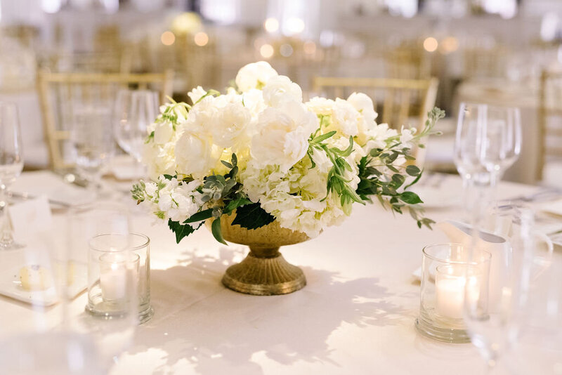 Lush white centerpiece in a gold footed vase with candles and crystal glassware, styled for an elegant Austin wedding reception.
