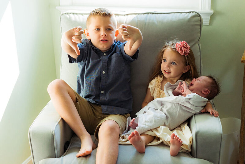A kid does thumbs down hands next to their two siblings.