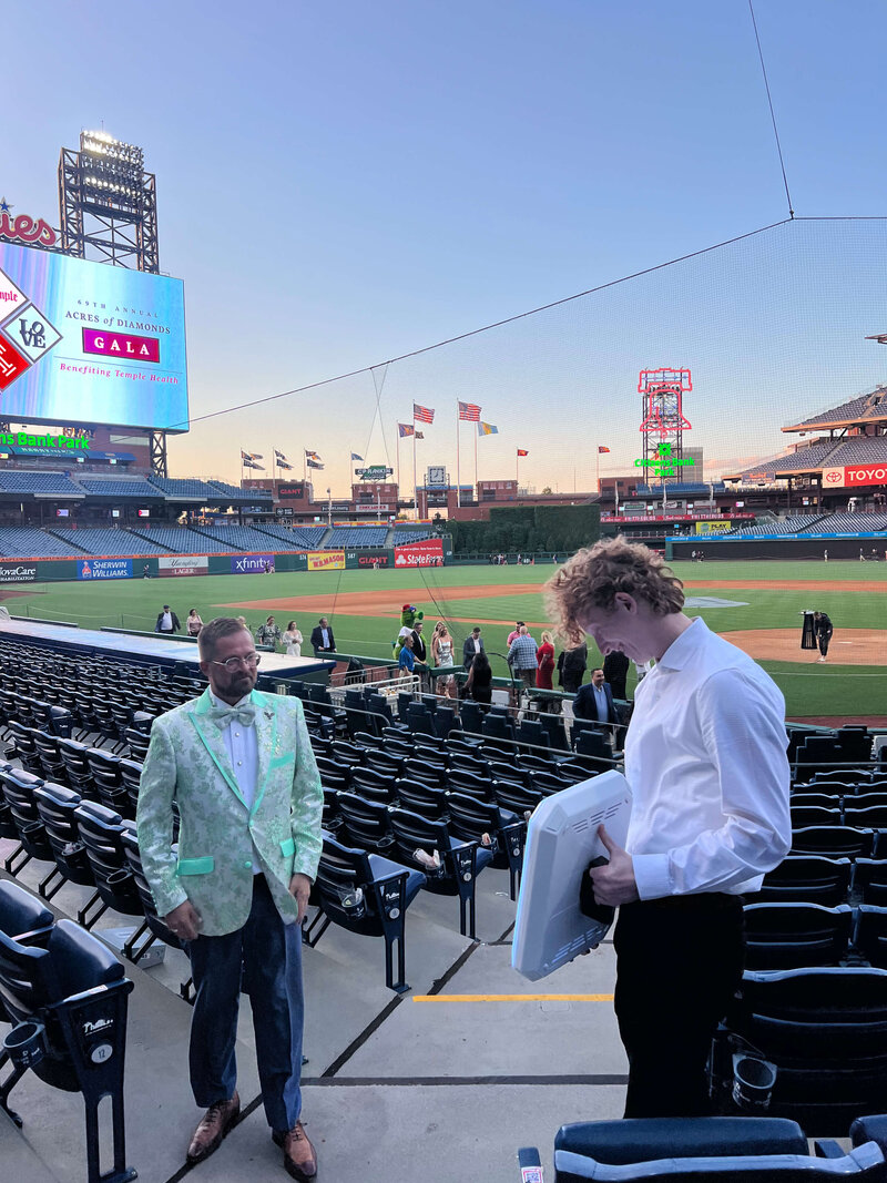 Roaming photo booth attendant engaging with a guest on the field at a stadium event, using a handheld booth unit.