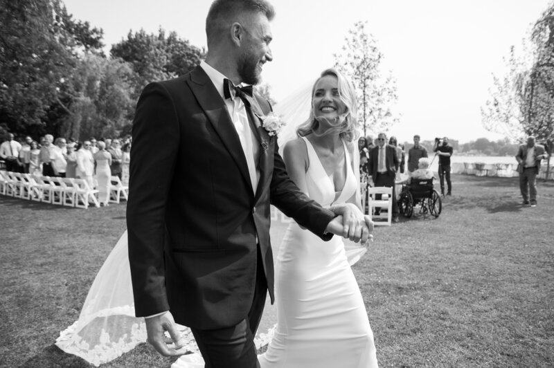 black and white photo of smiling bride and groom leaving ceremony