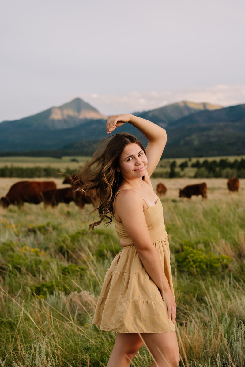 A girl posing in a cow pasture with mountains