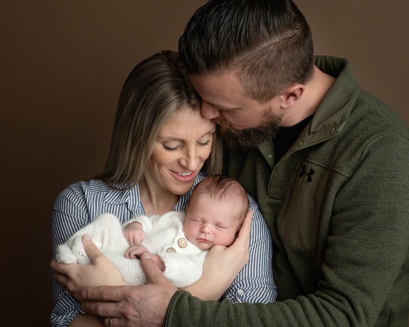 A timeless studio portrait celebrating the love and joy of new parenthood. This image features a newborn safely snuggled in their parents’ arms.
