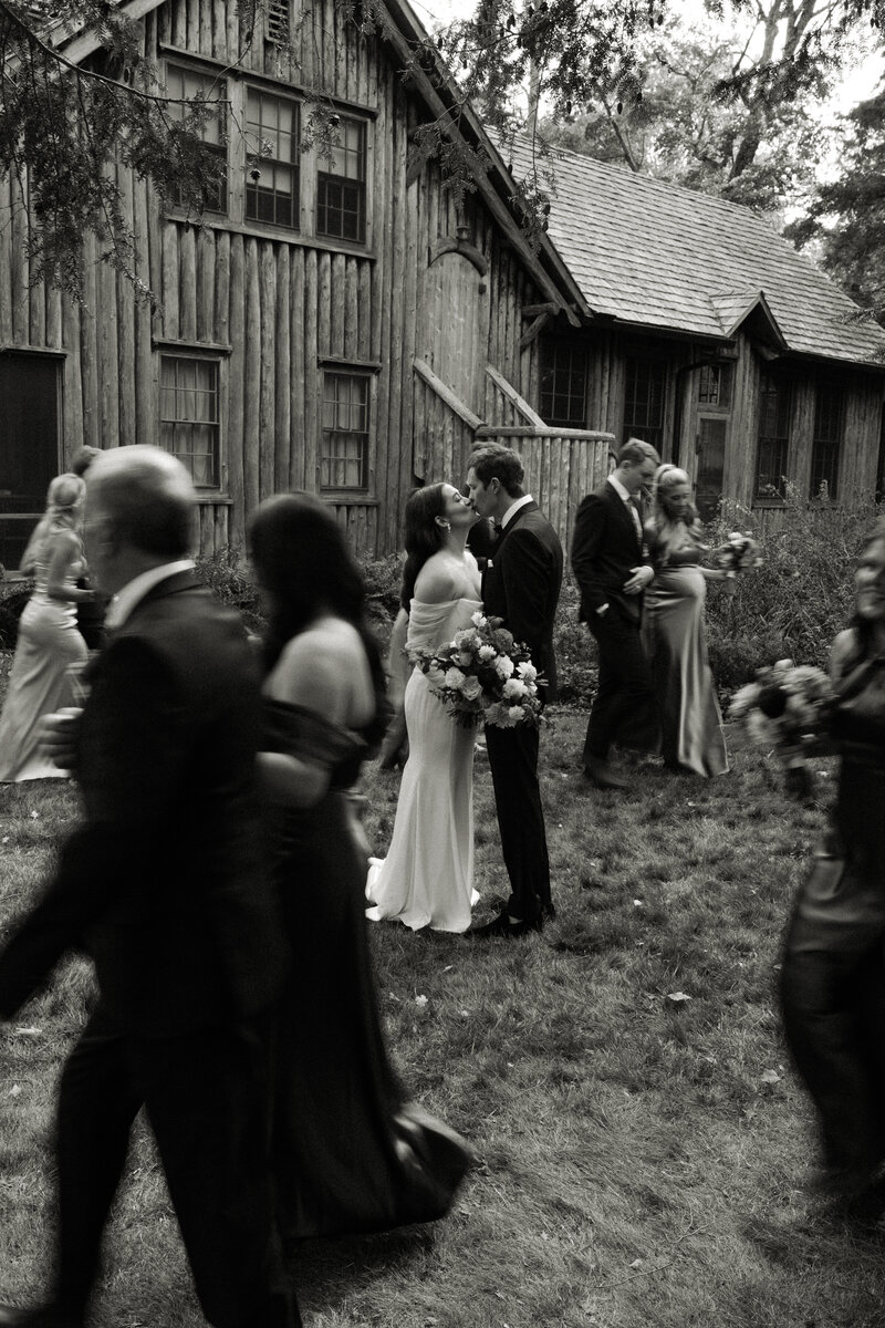 Bride and groom appear to be frozen in time as they kiss while their wedding party rushes around them.