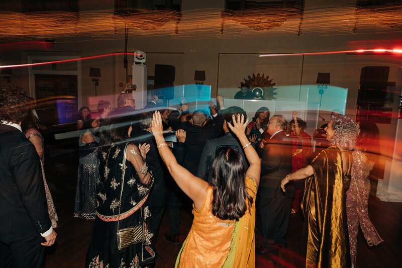 Wedding guests wearing wedding, Indian garments dance and celebrate on the dance floor.