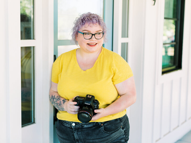 photographer in yellow shirt smiling and holding camera