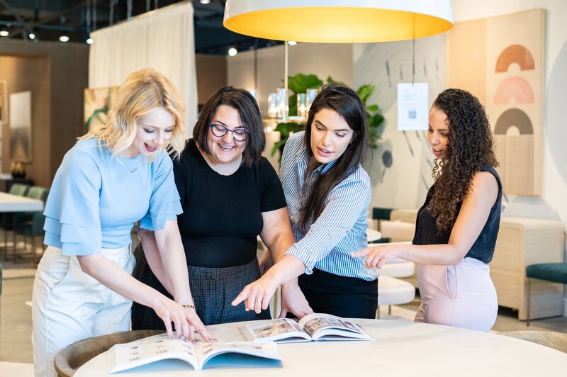 Three women, part of the interior design team, discussing plans around a table, all smiling and engaged