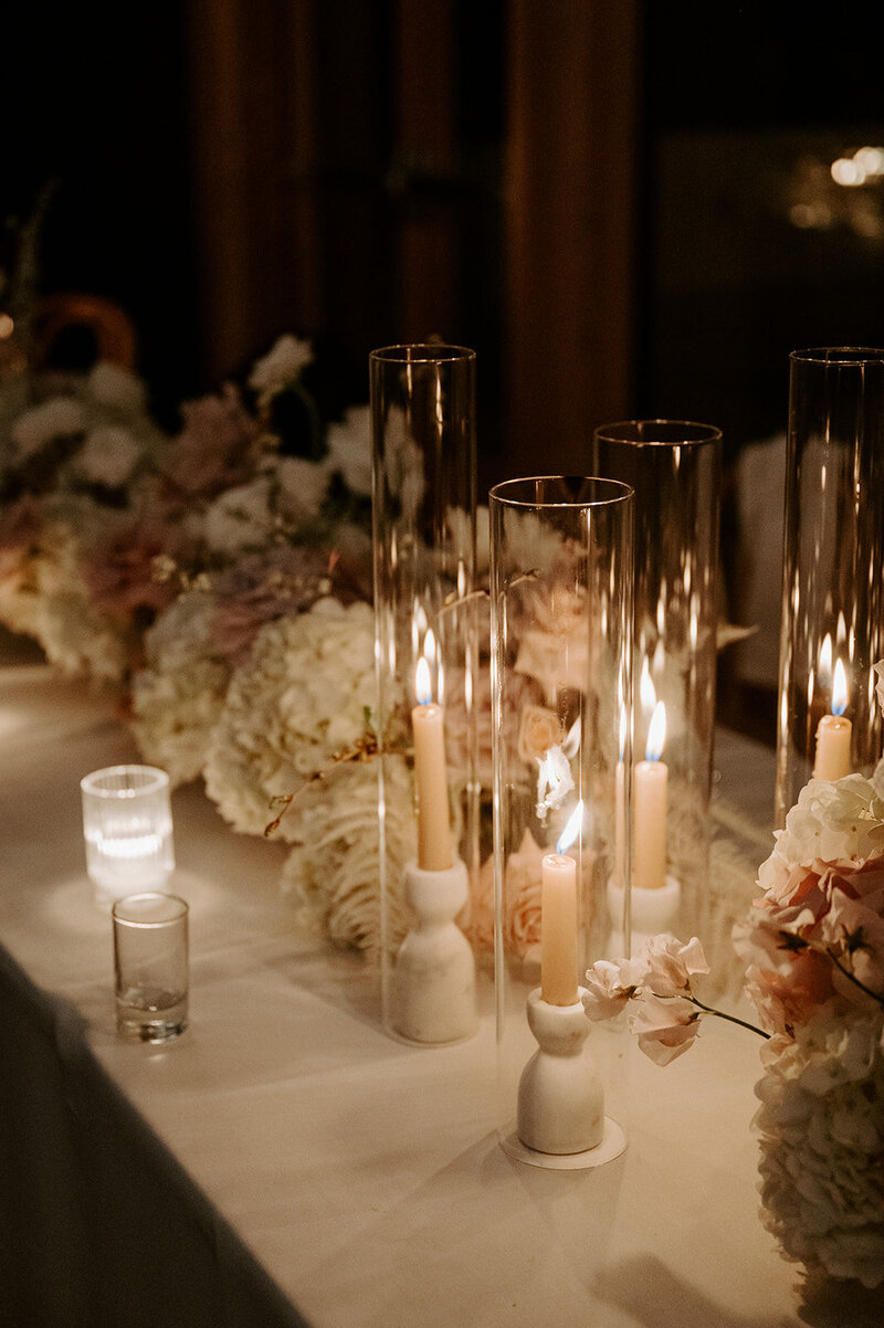 Close-up of reception table with white hydrangea, neutral roses, and bleached fern in lucite vases, styled with candlelight at Jenay and Daniel’s wedding by Summer Robbins Flowers in Central Oregon
