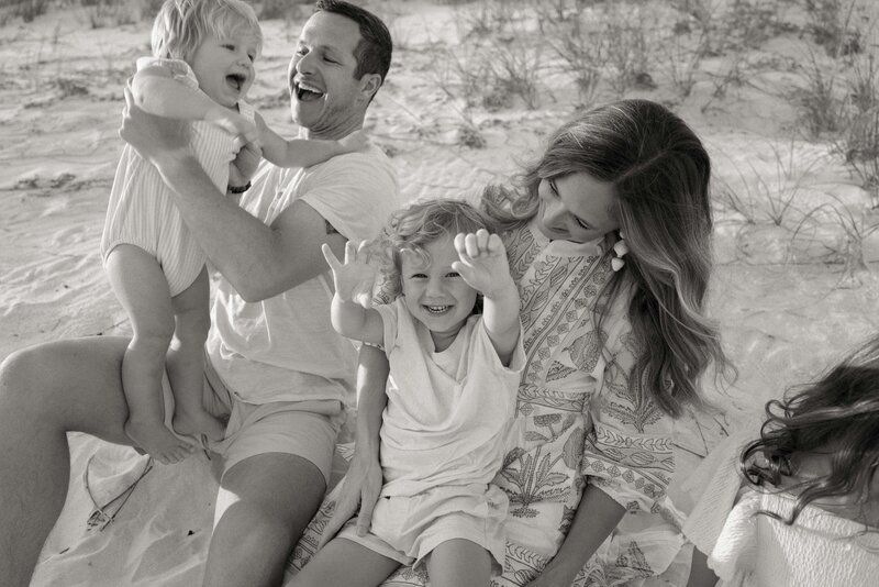 Black and white photo of family of four laughing while siting in the sand on the beach