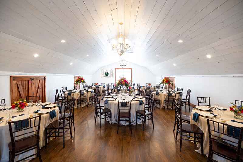 A loft space decorated for an event with lots of tables and chairs in the barn at Hidden Hill.